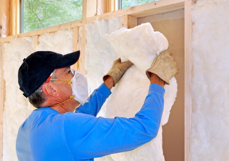 Man adding foam insulation to his home's carport