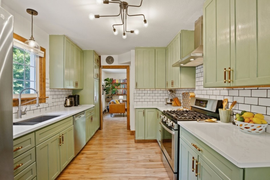A galley kitchen with cabinets painted green, wood floors, and white countertops