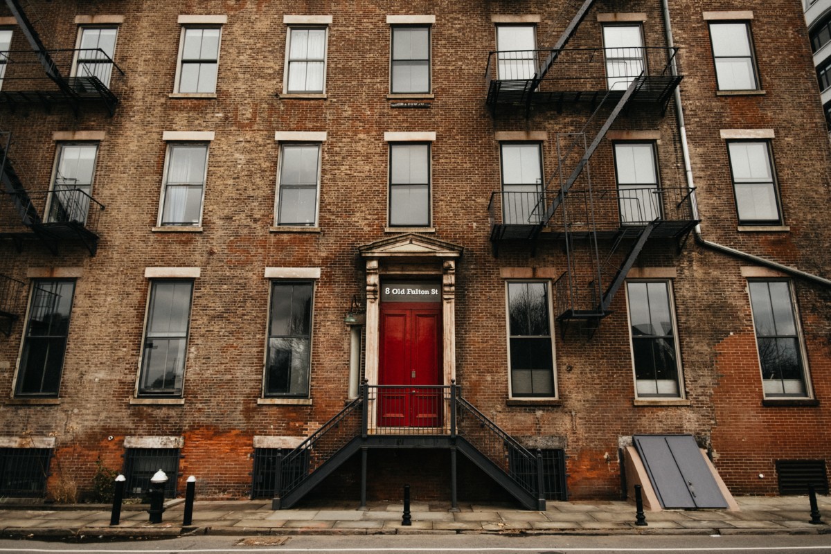 brown gothic revival row house with red door and many windows