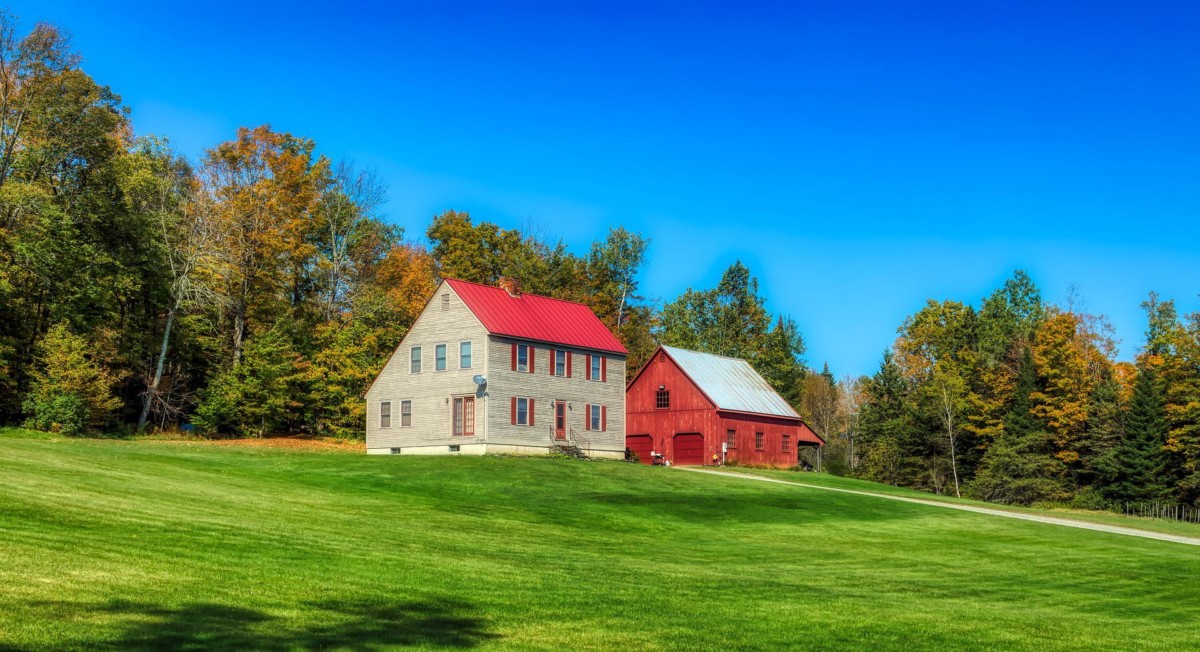 a saltbox home with a barn next to it in a field with red and grey sides