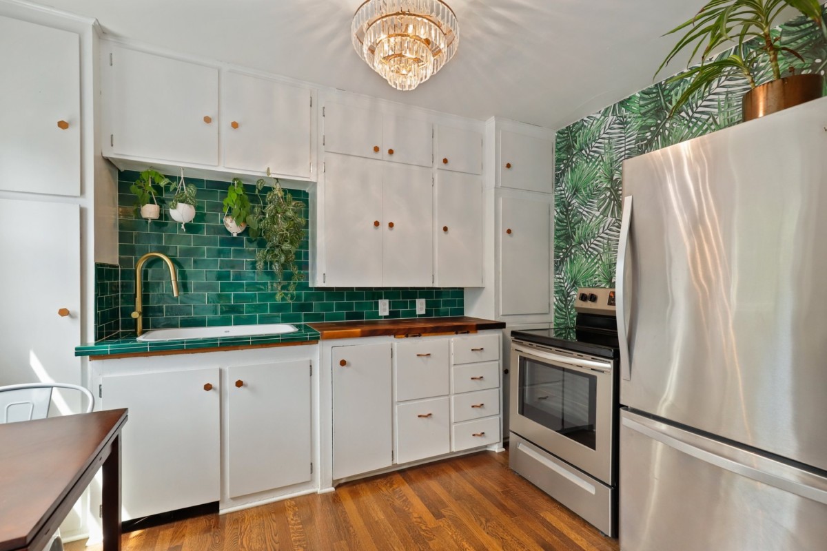 kitchen with a green tile backsplash, tropical accent wall, and white cabinets
