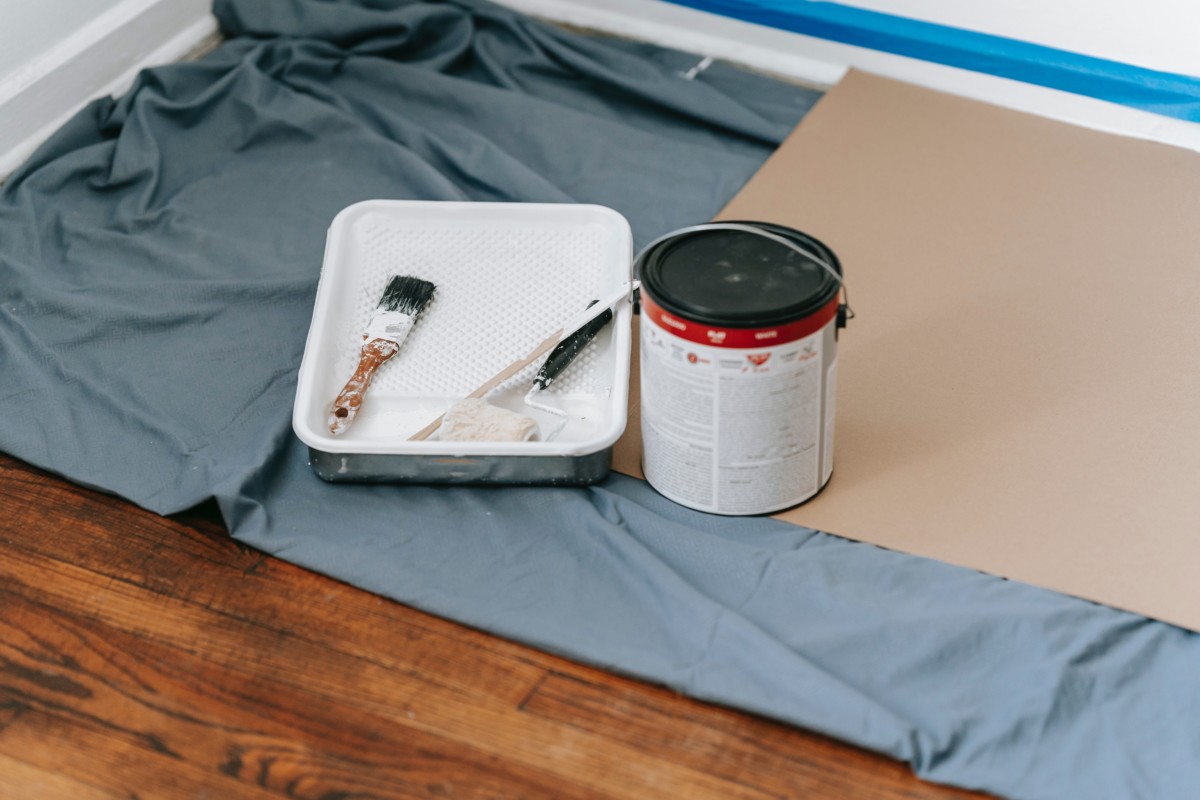 paint can and paint brushes on a tarp covering hardwood flooring
